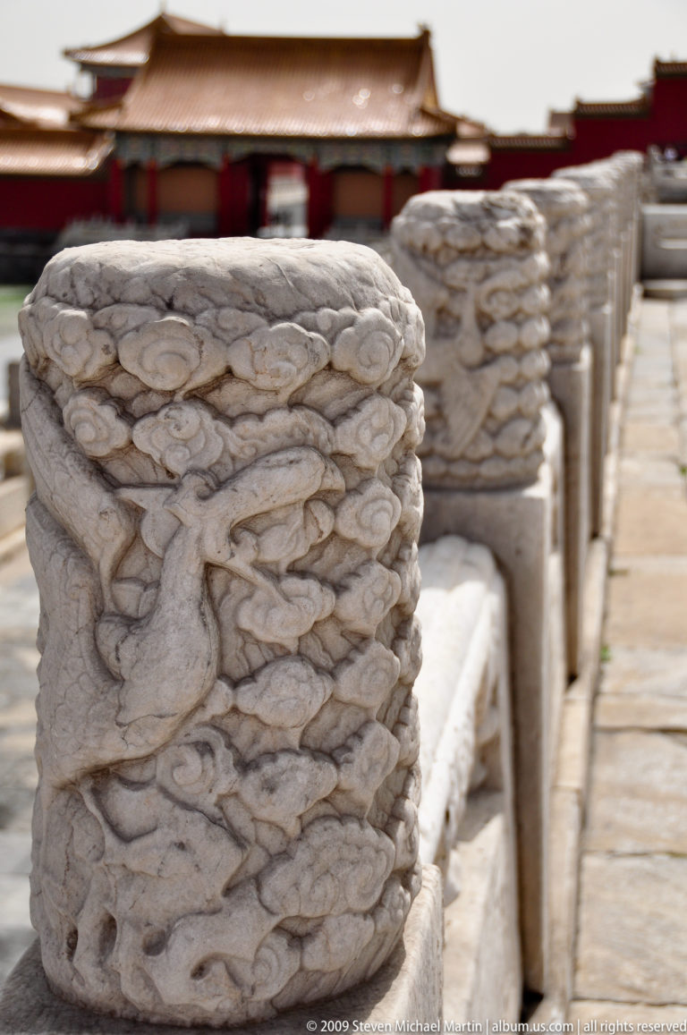 Close view of a stone baluster carved with a coiling dragon and cloud motifs, with similar posts receding in soft focus behind.