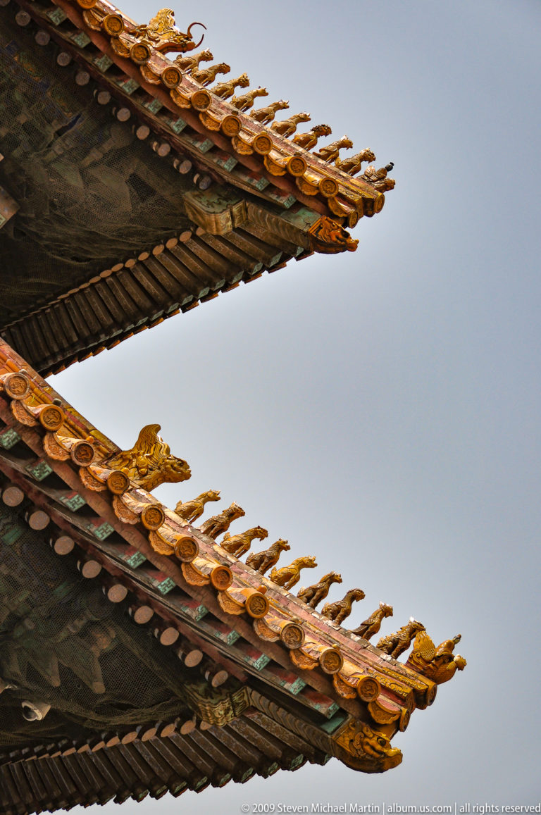 Two intersecting Forbidden City roof corners with small guardian figurines lining the yellow glazed ridge against the sky.