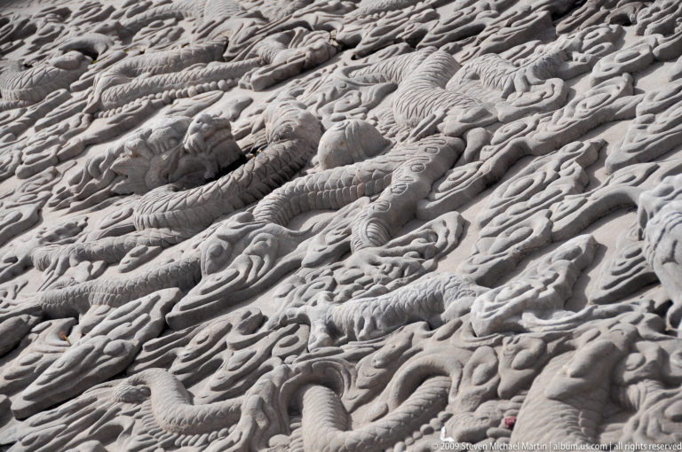 Oblique close view of a carved stone imperial ramp showing intertwined dragons amid dense cloud scrolls and wave patterns.