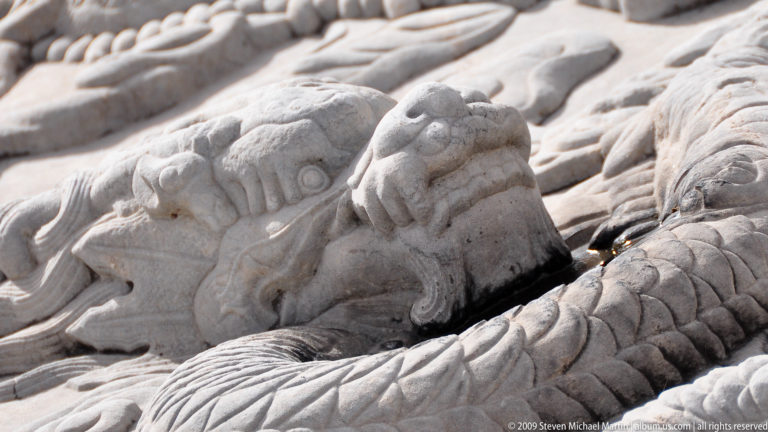 Close-up of a small carved lion or mythical beast set among scales and cloud motifs in a stone dragon-ramp relief.