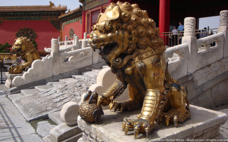 Gilt-bronze male guardian lion with one paw resting on a patterned brocade ball.