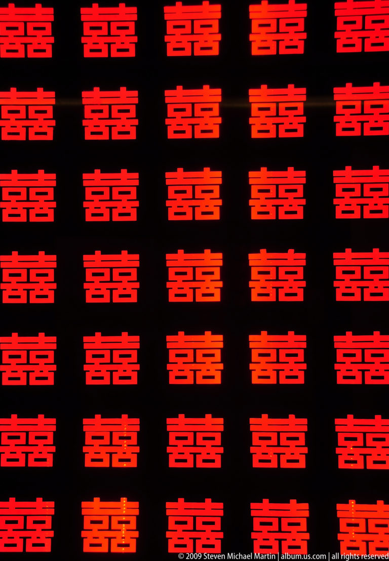 Pattern of bright red double-happiness Chinese characters repeating evenly on a black background.