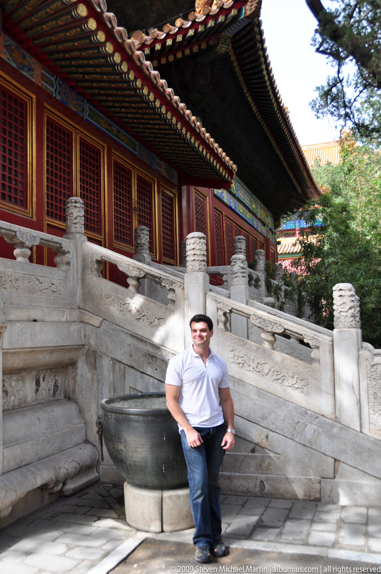 Male visitor standing beside a carved stone stair and red hall in an inner-court area of the Forbidden City.