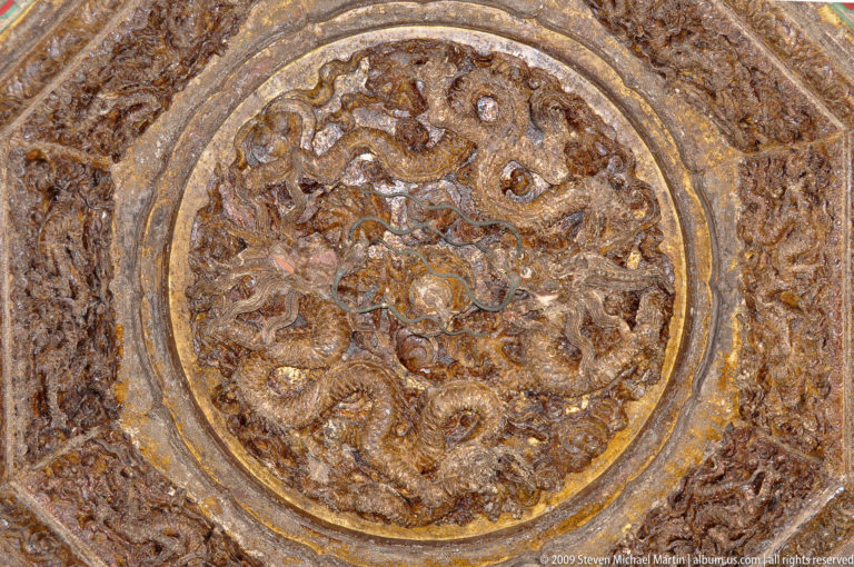 Close-up of a weathered circular dragon relief medallion with intertwined dragons in brown-gold tones.