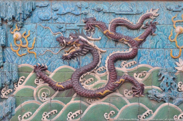 Purple five-clawed dragon in polychrome glazed relief above green waves on a turquoise panel from the Nine-Dragon Screen in the Forbidden City.