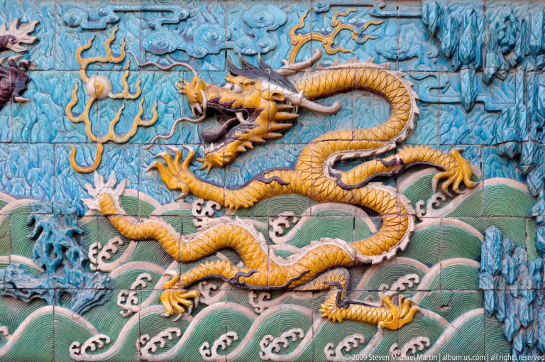 Yellow five-clawed dragon in polychrome glazed relief above green waves on a panel from the Nine-Dragon Screen in the Forbidden City.