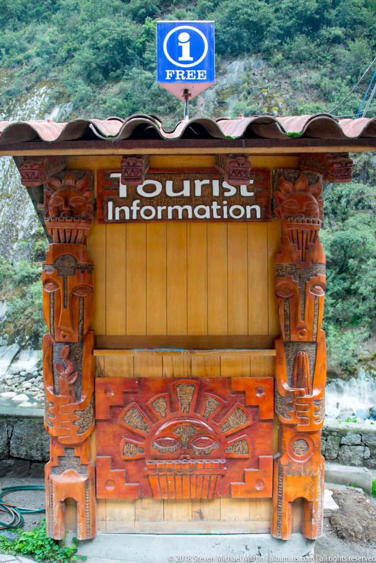 Carved wooden tourist-information kiosk with blue information sign and colorful Andean-inspired geometric panel.