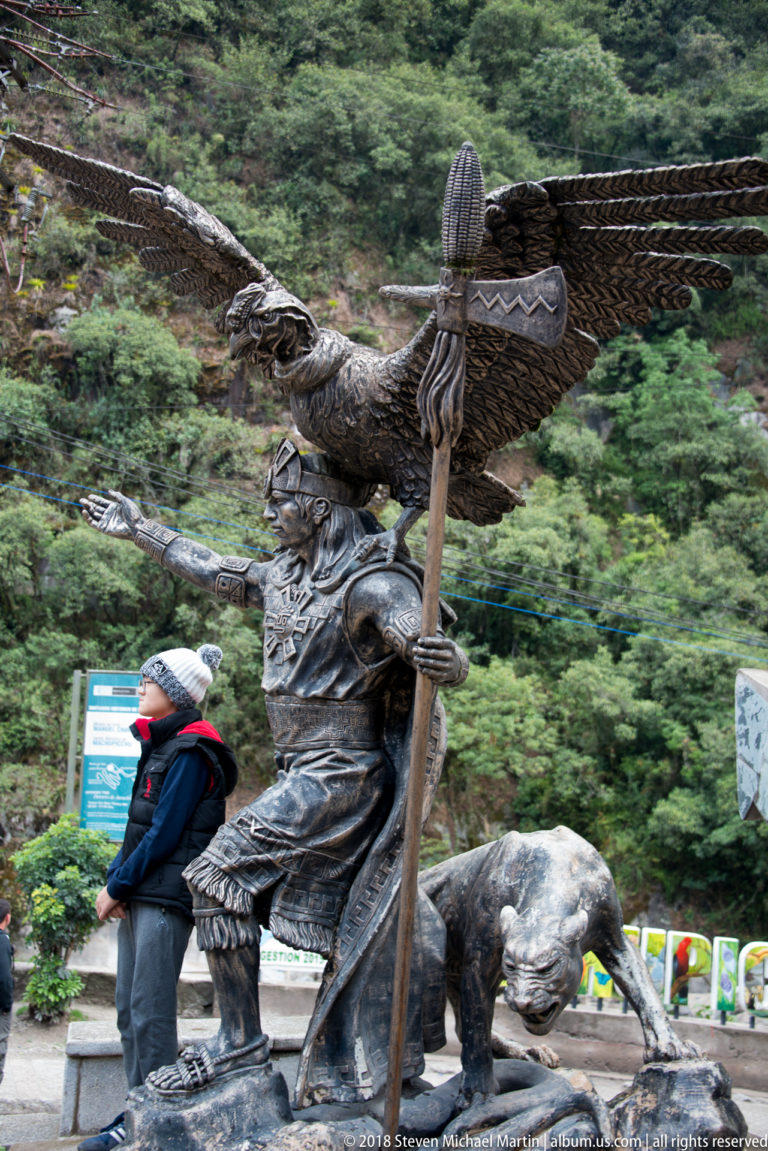 Bronze monument with a warrior holding a staff, a large bird above, and a crouching feline beside him.