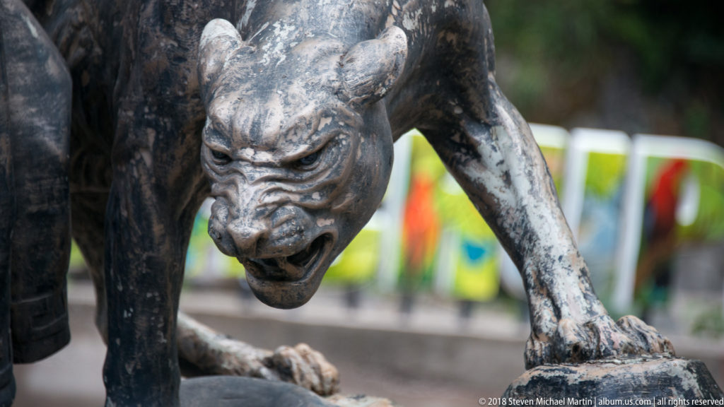 Close view of a snarling crouched bronze feline with muscular shoulders and bared teeth.