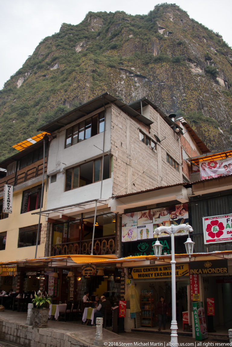 Row of multistory restaurants and lodging beneath a steep rocky, vegetation-covered mountain slope.