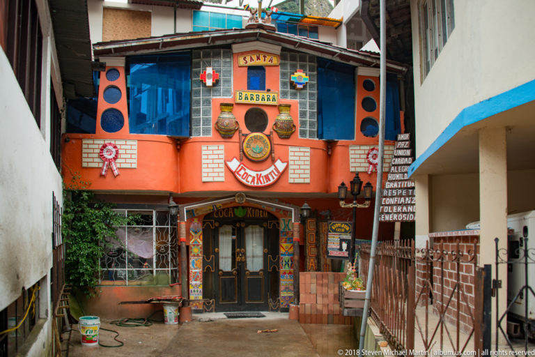 Bright orange-and-blue façade labeled Santa Barbara and Coca Kintu, decorated with masks and Andean-inspired motifs.