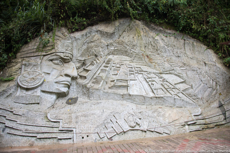 Pale stone relief with a profile figure in ornate headgear beside stepped geometric architectural forms.