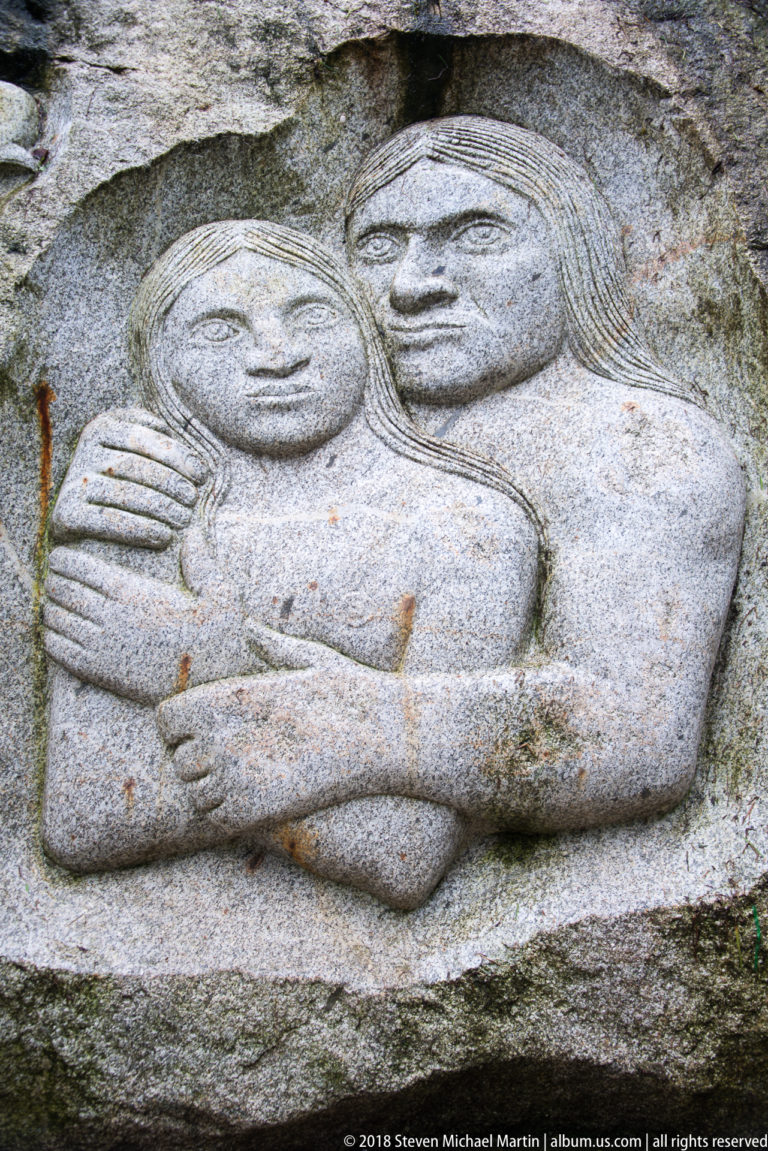 Stone relief of two reclining human figures embracing, carved into a rough rock surface.