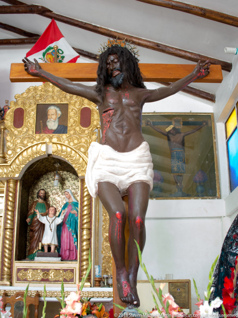 Life-size crucified Christ beside a gilded church retable containing a smaller painted religious scene.