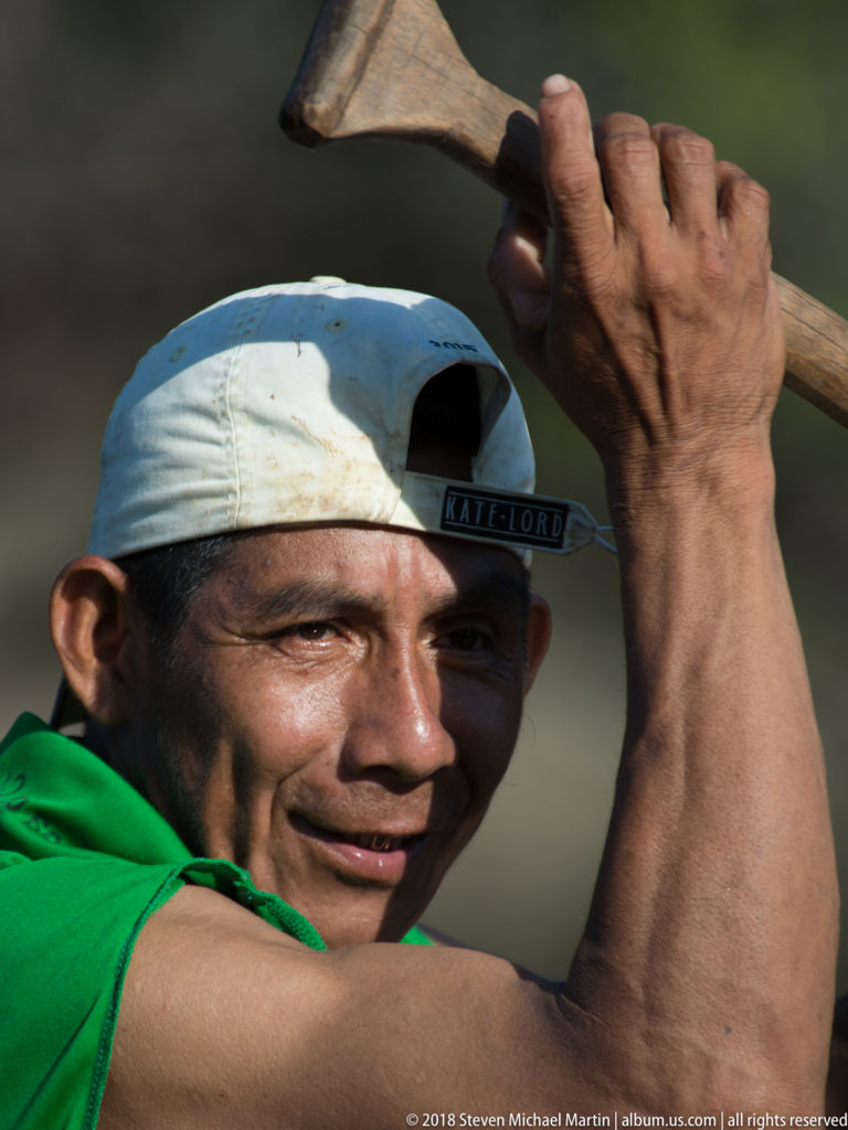 Close portrait of a canoe paddler holding a wooden paddle above his shoulder, lit from the side against a blurred background.