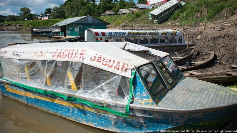 Covered motor launch marked JAGUAR moored beside narrow boats at a muddy Amazon River landing.