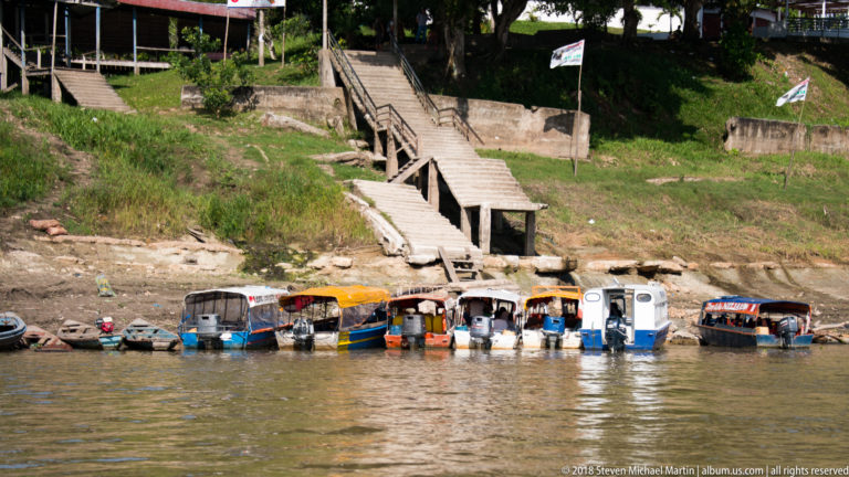 Row of small covered motorboats moored at a muddy Tamshiyacu riverbank beneath a long wooden stairway.