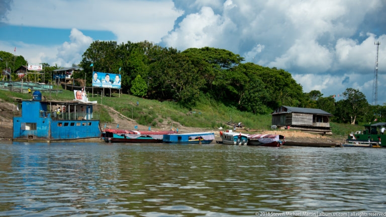 Several work and passenger boats moored below the green riverbank settlement of Tamshiyacu, Peru.