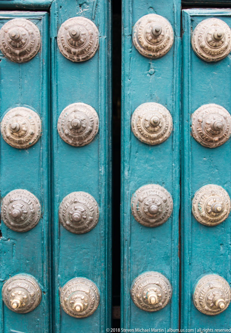 Close view of a turquoise wooden door covered with rows of round decorative metal bosses.