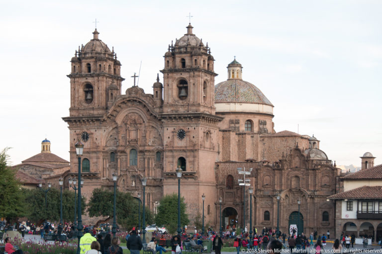 Ornate twin-towered façade and dome of the Iglesia de la Compañía de Jesús facing Cusco’s crowded Plaza de Armas.