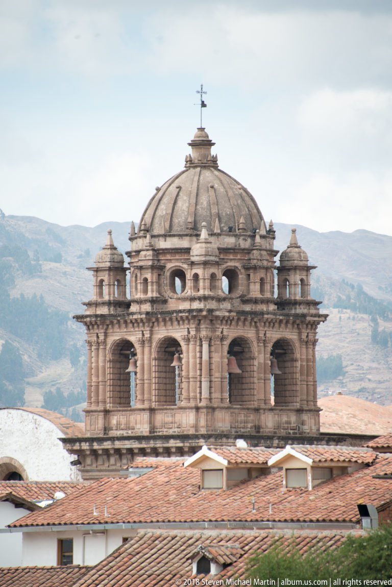 Large ribbed stone dome above an ornate arcaded drum and red-tile roofs, with Andean hills behind.
