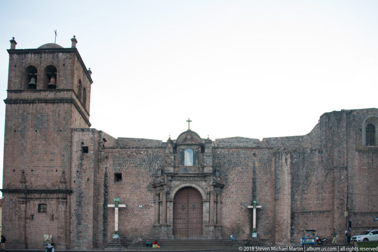 Large stone church with a tall square bell tower, broad plain façade and carved central entrance portal.
