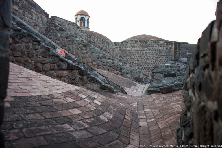 Brick-paved ramp curving between rough stone walls, with a small cupola visible above the masonry.