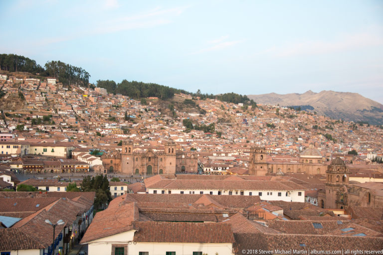 Cusco cathedral complex and red-tiled historic-center roofs below a densely settled hillside.