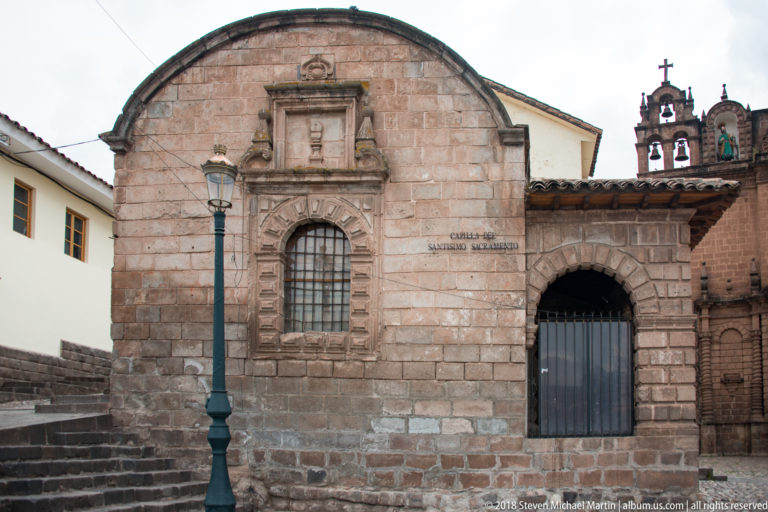 Stone façade of the Capilla del Santísimo Sacramento with barred window and gated arched passage.