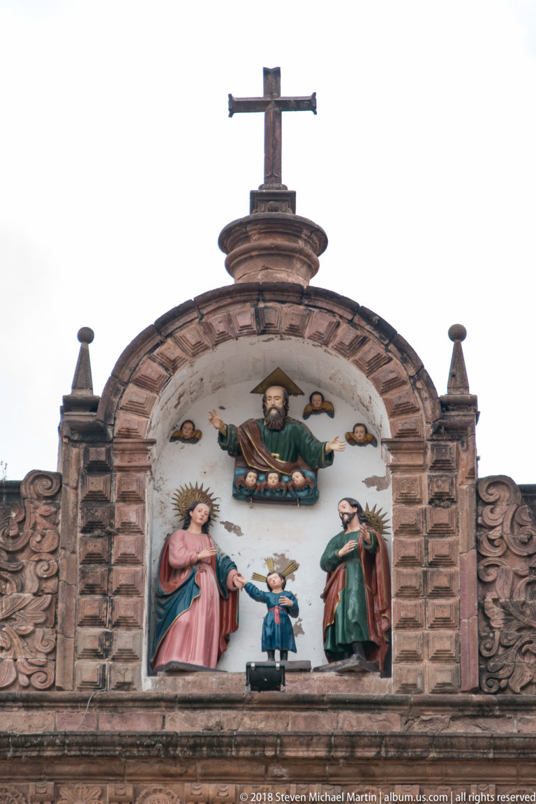 Polychrome religious group with two women, a smaller central figure, and a bearded figure above beneath a cross.