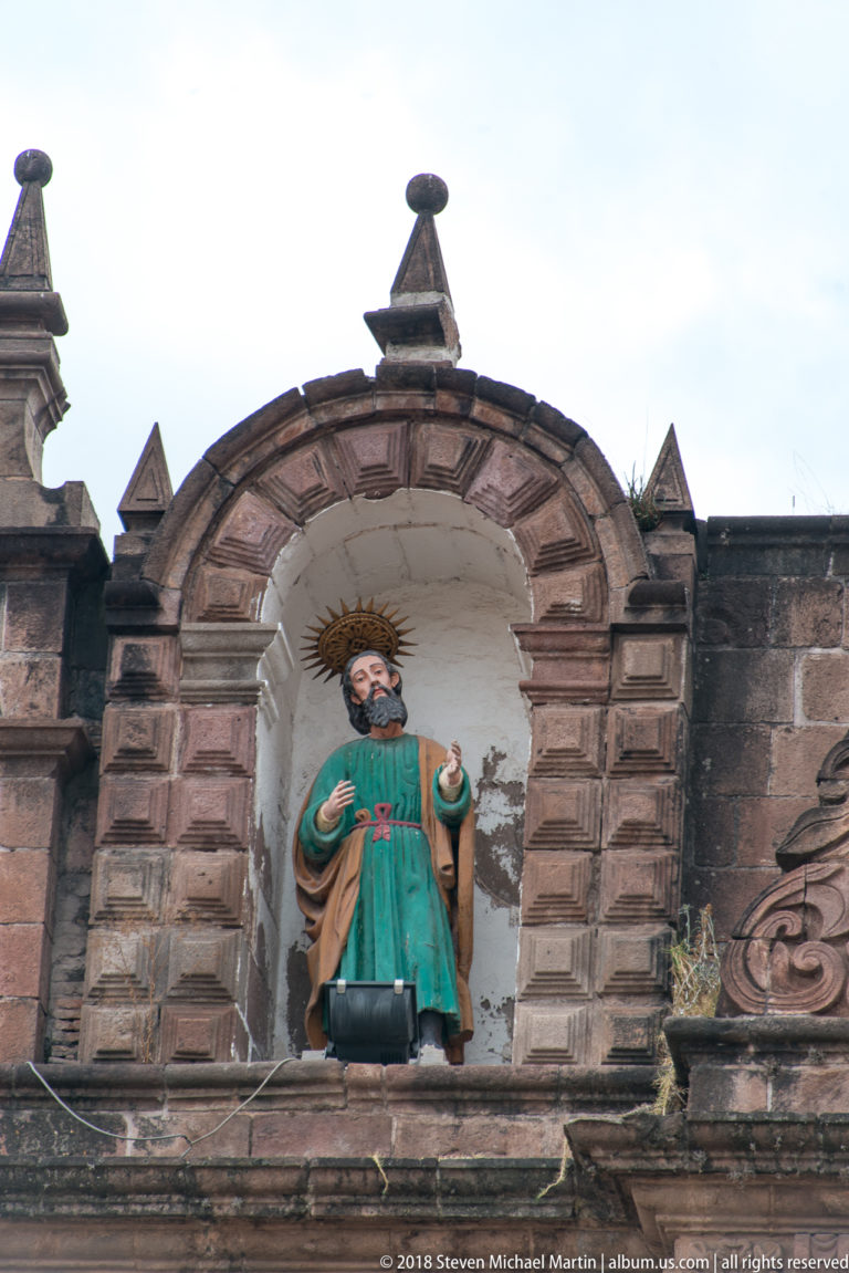 Polychrome bearded haloed male saint in turquoise and ochre garments within an arched niche.