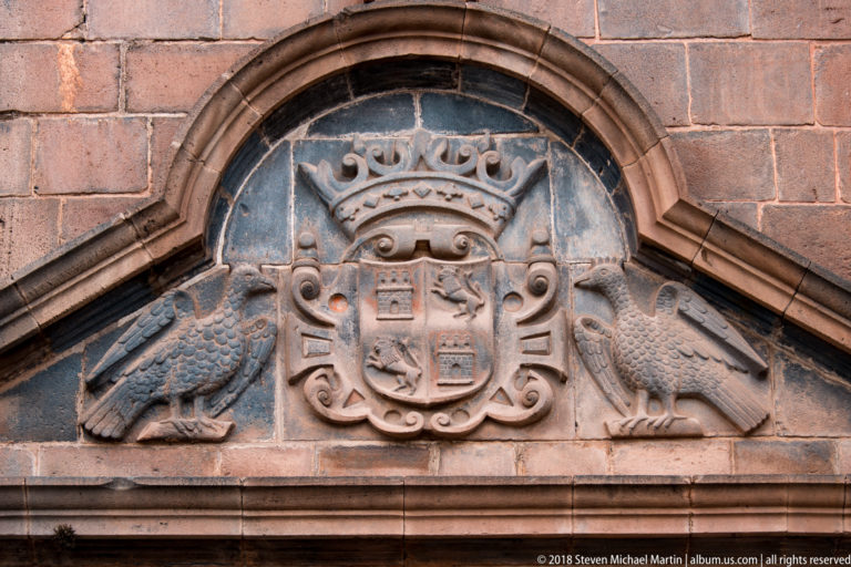 Crowned carved coat of arms flanked by two birds within a curved stone pediment.