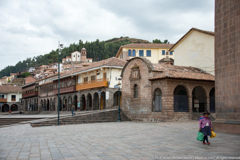 Stone chapel-like building and arcaded colonial façades beside a paved square in Cusco.