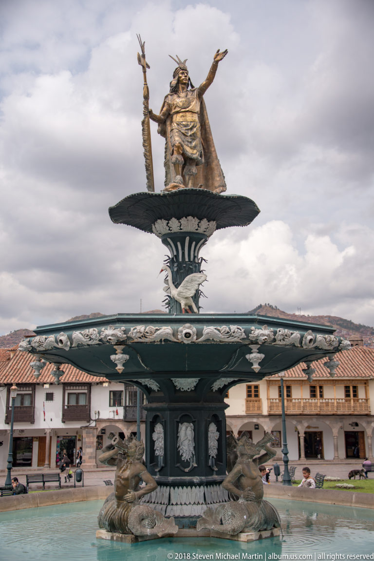 Multi-tiered Plaza de Armas fountain topped by an Inca ruler statue and ringed with sculpted figures.