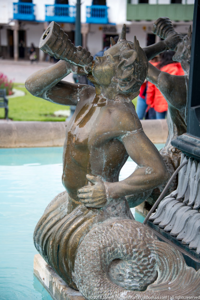 Bronze mermaid in profile with raised arm and coiled tail on the Plaza de Armas fountain.