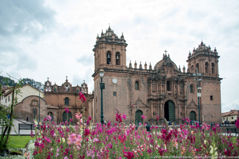 Cusco Cathedral with twin towers behind bright pink flowers in the Plaza de Armas.