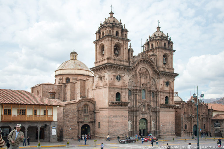 Closer view of an ornate twin-towered stone church with dome and pedestrians at its base.