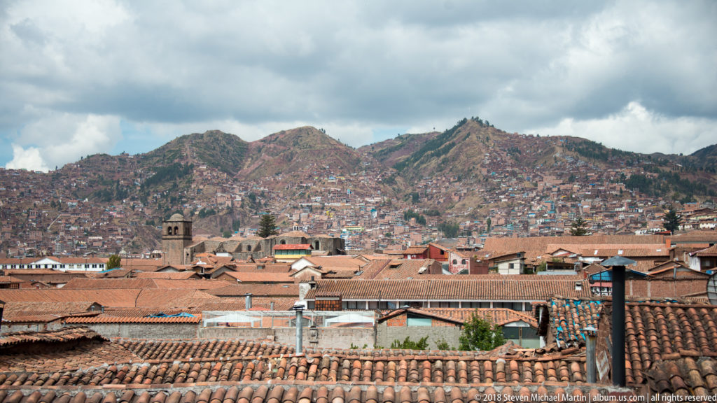 Red-tile roofs and a small church tower below densely built mountains under gray clouds.