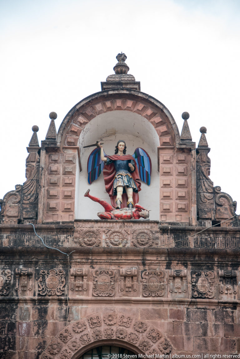 Polychrome winged religious figure standing in an arched niche above an ornate stone façade.