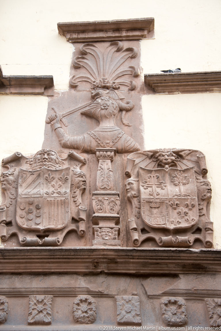 Large carved stone heraldic composition with several shields, scrollwork, and a central crest.