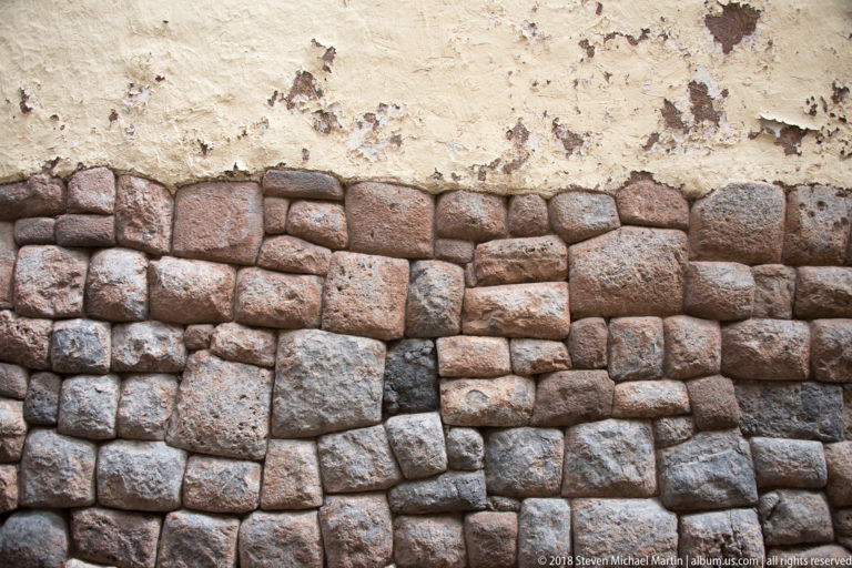 Polygonal fitted stone masonry forming the lower wall beneath worn yellow-white plaster.