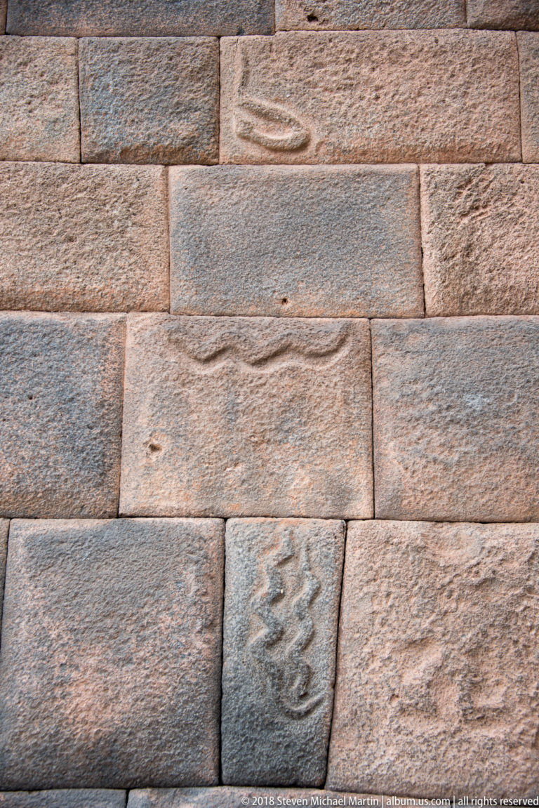 Close-up of fitted stone courses containing small carved wavy, zigzag, and oval motifs.