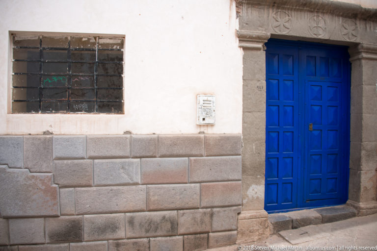 Blue wooden door and barred window above a wall of tightly fitted polygonal stone blocks.