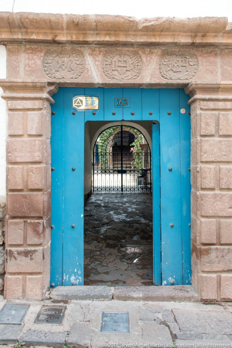 Bright blue double doorway in a carved stone portal, with a small arched opening revealing a courtyard gate.