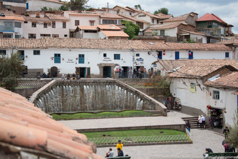 Elevated view of a long stone water wall, flanking stairs, tiled roofs, and pedestrians.