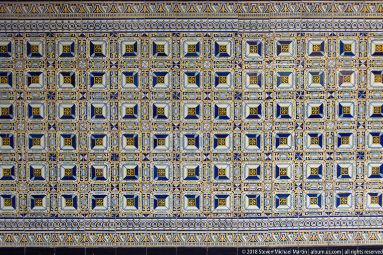 Close view of blue, yellow, white, and black ceramic tiles arranged in repeating square geometric patterns.