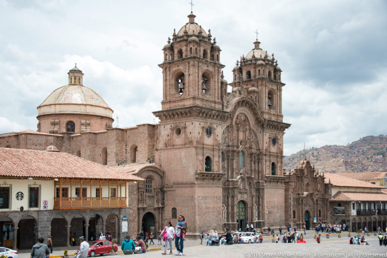 Cusco’s Jesuit church with ornate twin-towered façade, large dome, plaza activity, and arcaded buildings.
