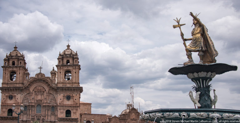 Inca ruler statue atop the Plaza de Armas fountain with the twin-towered Jesuit church behind.