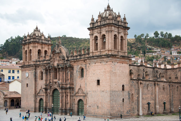 Cusco Cathedral with twin towers and ornate façade, seen across the plaza with hillside neighborhoods behind.