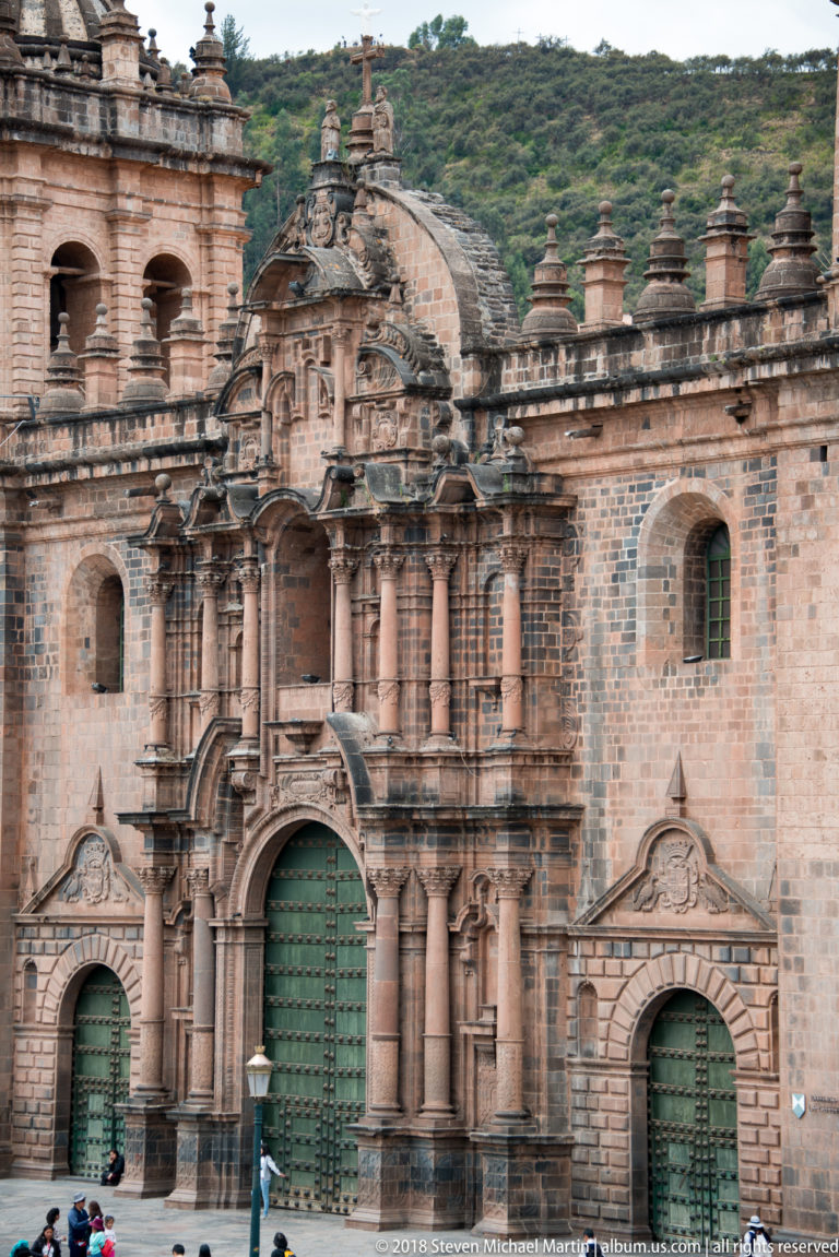 Central stone façade of Cusco Cathedral with three green doors, columns, niches, and ornate baroque detailing.